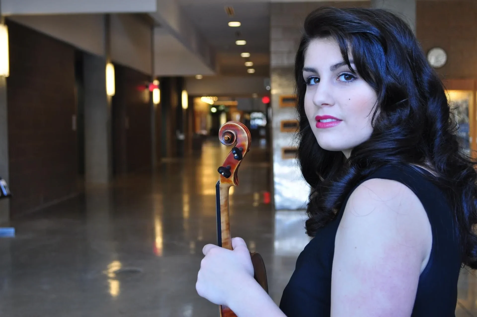 A woman holding a violin in an empty room.