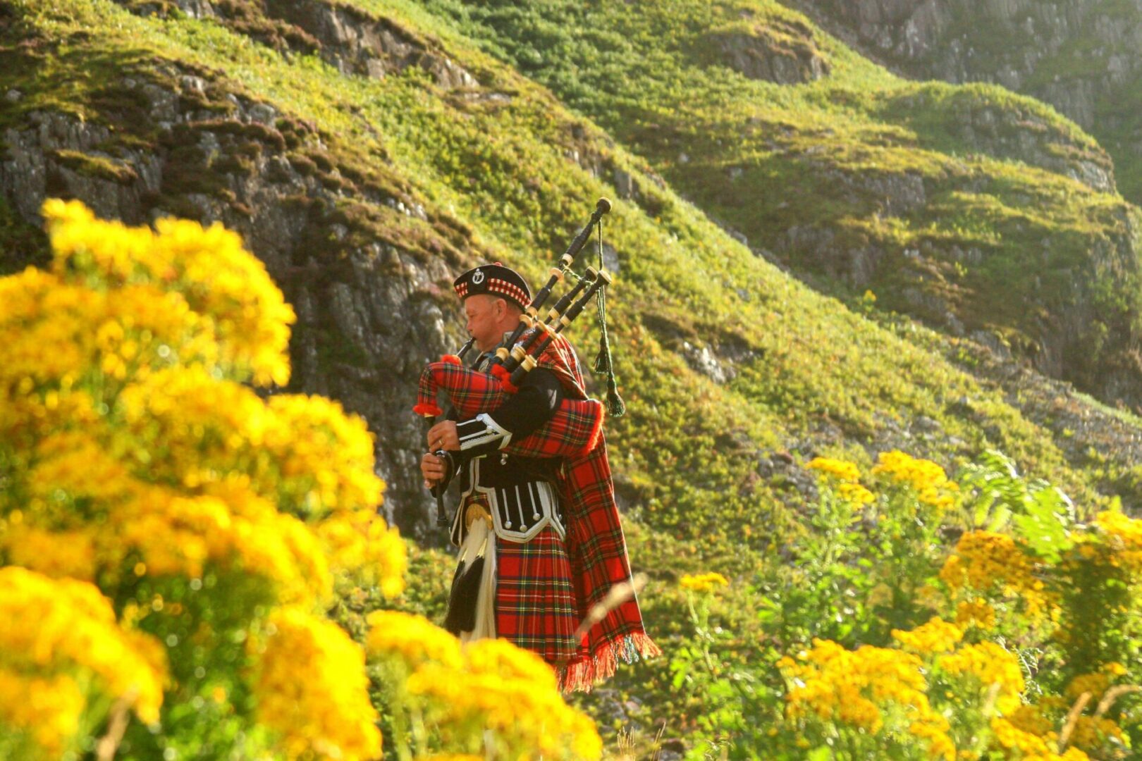 A man in red plaid coat playing the bagpipes.