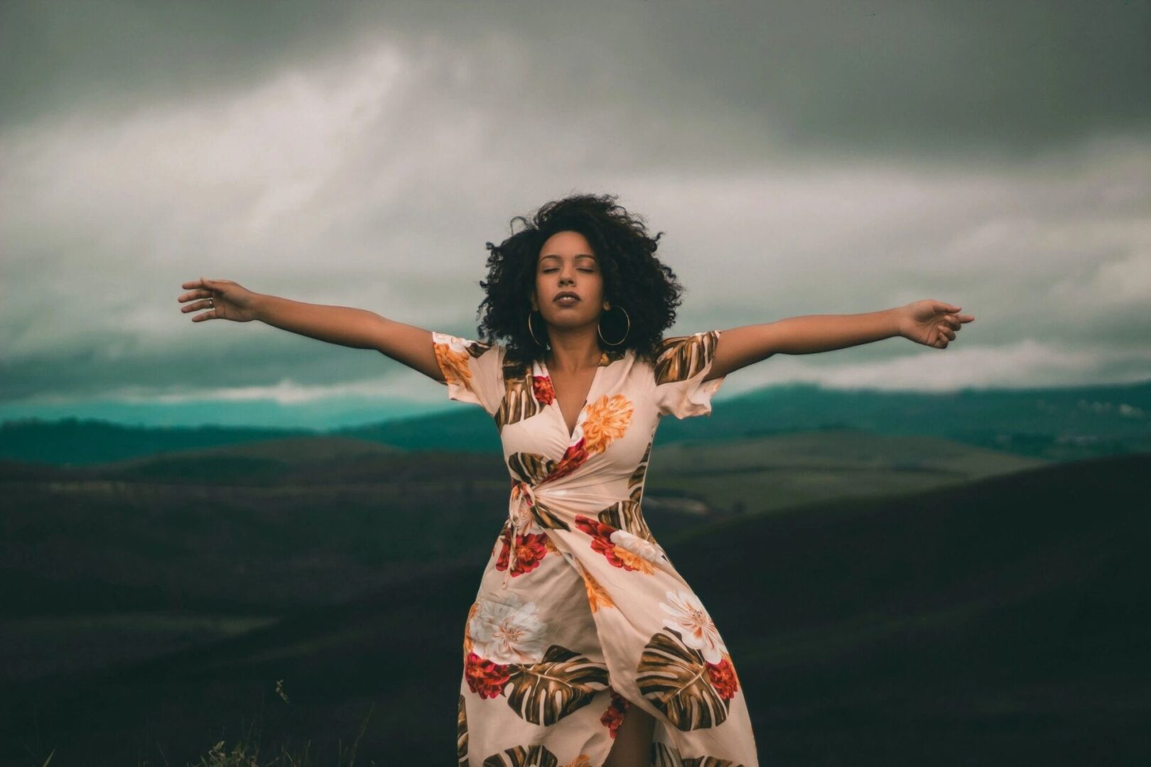 A woman in floral dress standing on top of hill.