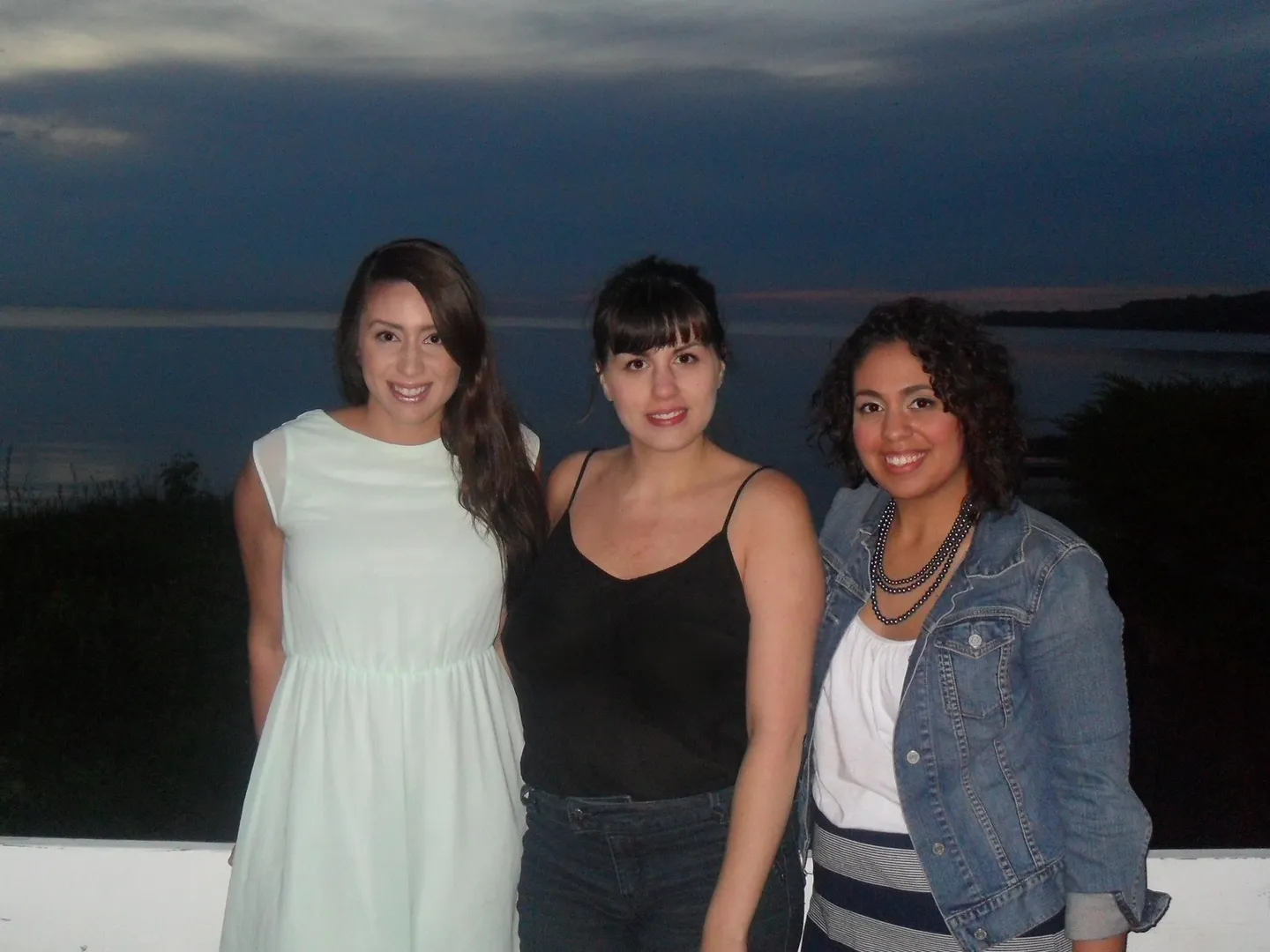 Three women standing next to each other in front of a body of water.